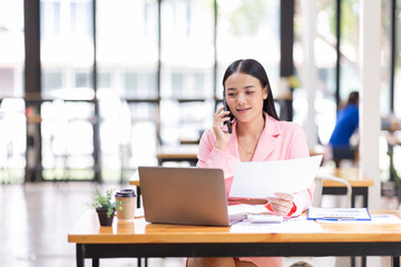 Young Business Asian woman talking on a smartphone and working in an office. Asian female Business finance sitting at his workplace.