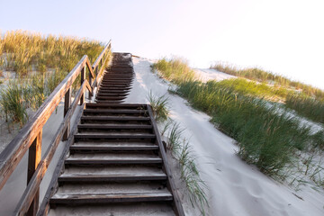 Wooden stairs on sand dune covered with grass, way to the entrance of the beach. Coastal landscape by morning light. Baltic sea.