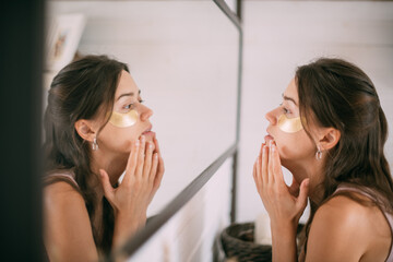 Young woman with patches under her eyes at the mirror at home.