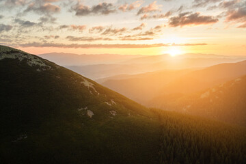 Aerial view of amazing scenery with foggy dark mountain peak covered with forest pine trees at autumn sunrise. Beautiful wild woodland with shining rays of light at dawn