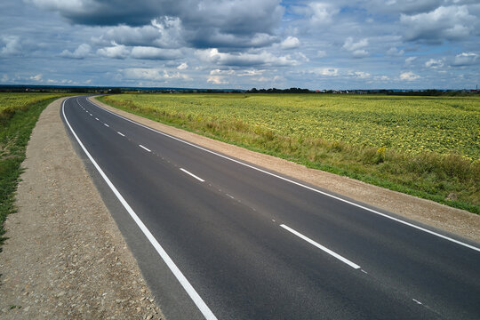 Aerial view of empty intercity road between green agricultural fields. Top view from drone of highway roadway
