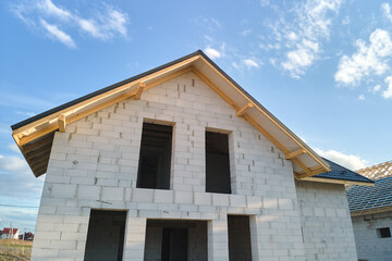 Aerial view of unfinished house with aerated lightweight concrete walls and wooden roof frame covered with metallic tiles under construction