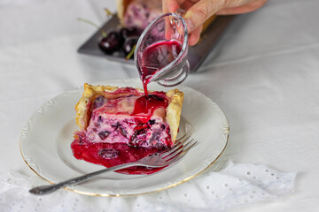 Female hand pouring cherry syrup over a puff pastry, ricotta and cherry cake.