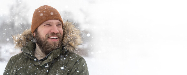 Closeup mature man bearded winter coat with fur collar and brown knitted hat snow outdoor. Positive...