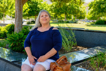 Mature white woman sitting on a city park with a big smile