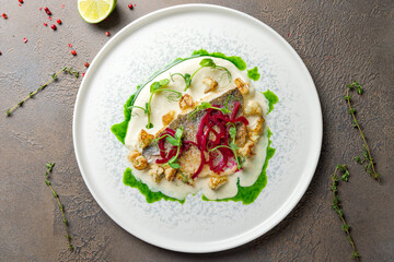 Dorado on grill on plate with sauce and red marinated onion on brown table