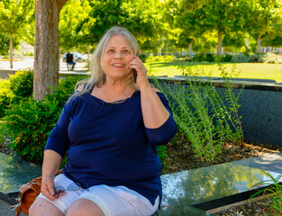 Elderly white woman sitting outdoors talking on her phone.