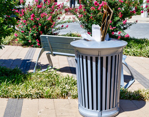 Beautiful city park with a stylish trash recepticle full of trash.