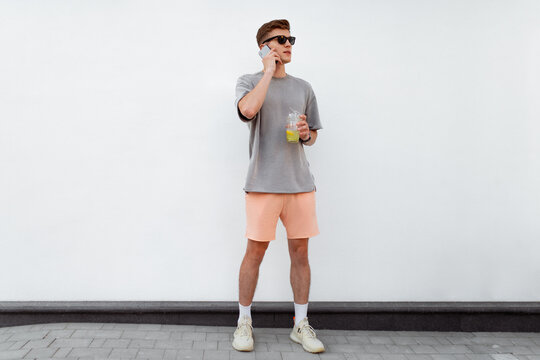 Portrait of handsome confident stylish hipster man in sunglasses talking on the phone, standing guy near the concrete wall. Calm relaxing moment, summer vacation concept