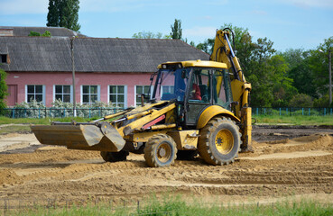 Obraz premium a yellow tractor with a blade and a bucket levels the sand at a construction site. construction machinery doing hard work