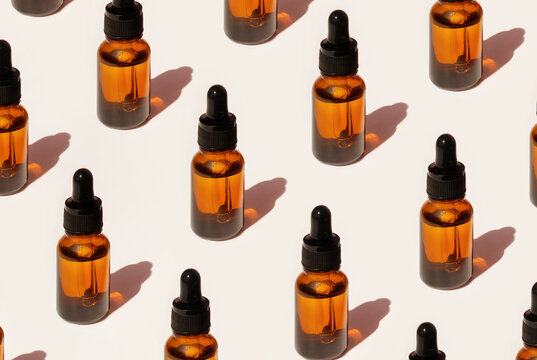 Pattern of Transparent amber green glass dropper bottles with liquid inside on beige background in the sunlight. Pipette with fluid hyaluronic acid, serum, retinol. Cosmetics, healthcare, beauty 