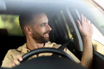 Confident smiling taxi driver waving hand waiting for client sitting in car. Transportation concept 