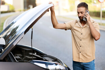 Sad driver calling car service, opening hood, having engine problem standing near broken car on the...