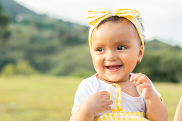 beautiful brown-skinned latina baby in an outdoor field on a summer day, smiling and showing her...