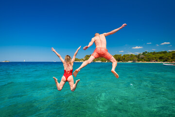 A carefree couple jumps into the azure sea. A vacation in the summertime. Young and energetic people dive into the water together. A fun vacation at the sea together.