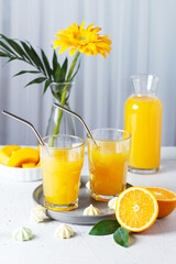 Glasses with orange juice, orange slices and mango on a gray background.