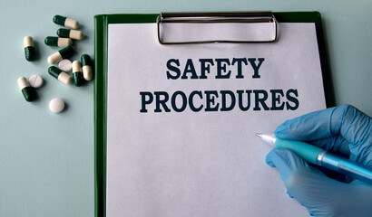 SAFETY PROCEDURES - words on a white sheet on the background of a hand in a blue glove with a pen and tablets