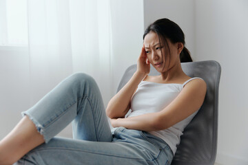 Migraine. Side view of unhappy suffering from headache tanned beautiful young Asian woman touching forehead at home interior living room. Injuries Poor health Illness concept. Cool offer Banner