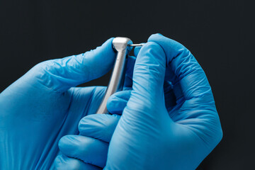 A close photo of a hands of a dentist who holds a dental high speed turbine in the turbine stainless handpiece.