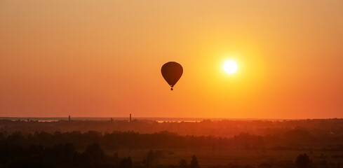 Colorful air balloon is flying in free flight over the field. Bird's-eye view. Multicolored balloon in the sky at sunset