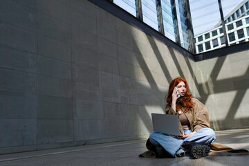 Teen redhead hipster girl student talking on cell phone using laptop computer modern technology...