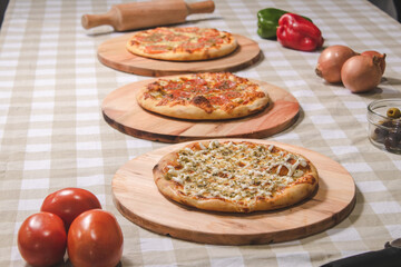 Three personal pizzas of different flavors on a table with a checkered tablecloth.