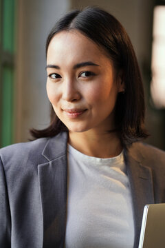 Smiling Young Elegant Successful Rich Professional Leader Asian Business Woman, Female Executive Manager Or Teacher Wearing Suit Holding Digital Tablet Looking At Camera, Vertical Headshot Portrait.