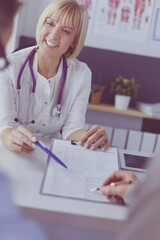 Doctor and patient examining a file with medical records, she is sitting on a wheelchair