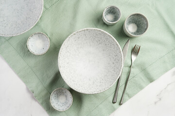 Empty grey ceramic scandy soup bowl, espresso coffee mugs and dip bowl, fork and knife on a marble surface and kitchen towel, top view