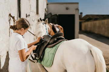 12-year-old girl tightening the saddle strap of a saddle