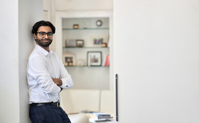 Naklejka na ściany i meble Smiling young rich successful indian business man ceo, arab professional manager, eastern businessman leader standing arms crossed looking at camera on white office wall background, portrait.