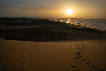 Fototapeta na wymiar Footsteps in the sand with dunes and sunset
