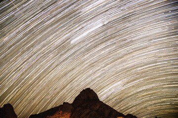 star trails behind a mountain in the desert of namibia