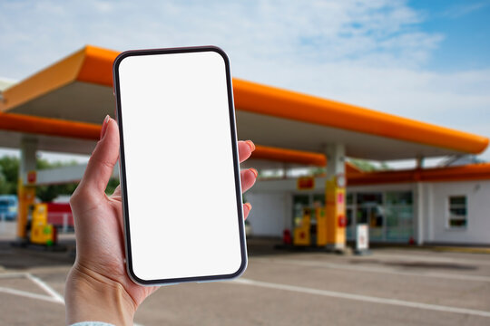 Woman holds a close-up of a smartphone with a white screen in his hands against the backdrop on a gas station. Technology mockup for apps and websites.