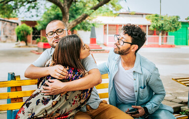 Disloyal girlfriend hugging her boyfriend in a park secretly kissing another man. Couple infidelity concept, Unfaithful woman sitting hugging her boyfriend and secretly kissing another man.