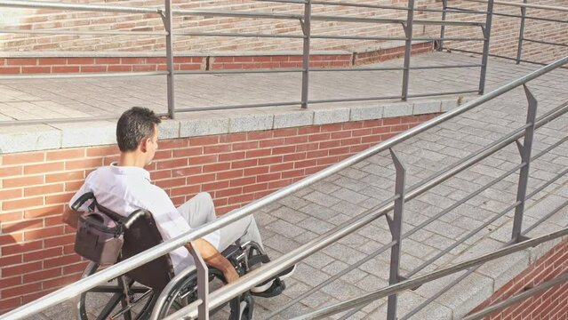 40-year-old man with dark skin in light clothing and black shoes in a wheelchair going up a ramp for the disabled