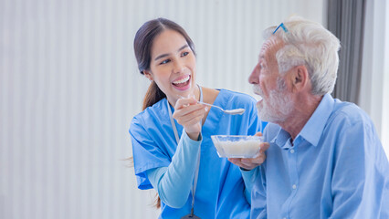 Hospice nurse is feeding porridge food to Caucasian man at pension retirement center for home care...