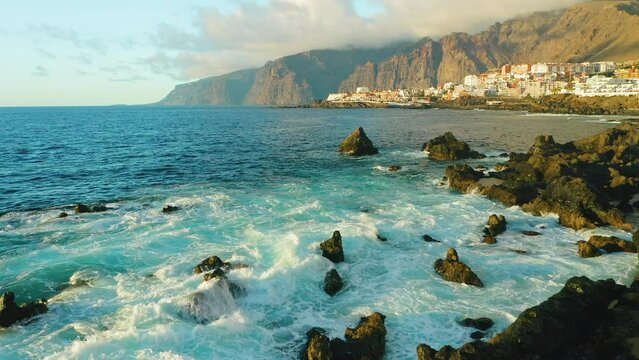 Touristic spot. Aerial sunset light on ocean waves and rocks. Tenerife, Canary Island, Los Gigantes cliffs, town Puerto de Santiago, natural pool of Devil. Lava flows, volcanic bizzare stone beach