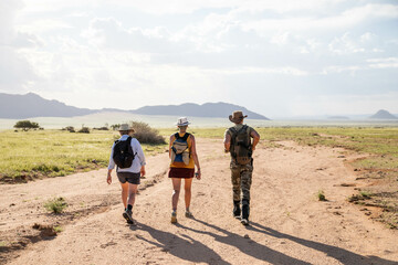 hikers in the namibia desert towards the mountains - obrazy, fototapety, plakaty