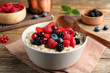 Bowl with tasty oatmeal porridge and berries served on wooden table. Healthy meal