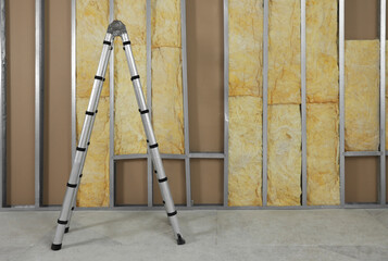 Ladder near wall with metal studs and insulation material indoors