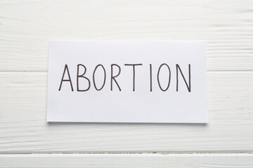 Paper note with word Abortion on white wooden background, top view