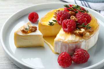 Brie cheese served with raspberries, walnuts and honey on white wooden table, closeup