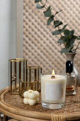 Fototapeta na wymiar Burning soy candle, perfume and stylish accessories on wicker table indoors