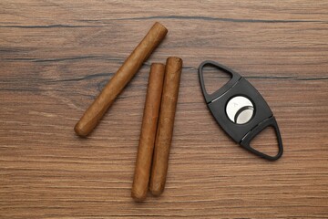 Cigars and guillotine cutter on wooden table, flat lay