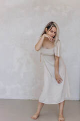 Fototapeta premium Girl in a linen dress and dried flowers near a white wall