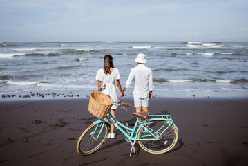 happy couple holding hand walking on black sandy beach together