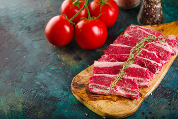 Appetizing meat steaks on a cutting board are waiting to be cooked. Ripe tomatoes on a marble dark background. Cooking meat dishes. Recipes for home cooking.