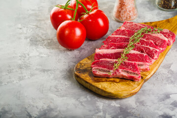 On a wooden cutting board, raw meat steaks, fresh tomatoes on a gray background. Meat recipes for home and restaurant cuisine. There are no people in the photo. There is free space to insert.