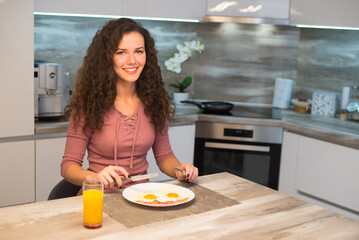 Young smiling woman eating fried eggs and bacon for breakfast